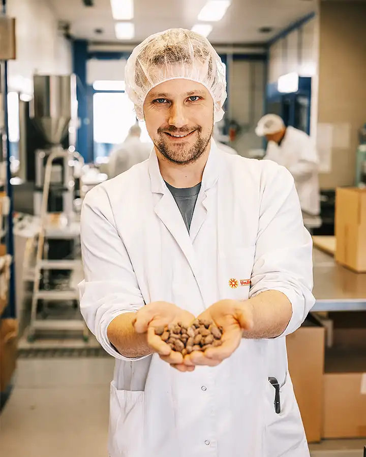 Mann mit hygienischer Schutzbekleidung präsentiert Kakaobohnen auf Händen