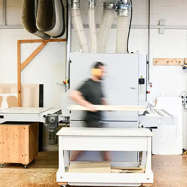 Schreiner mit Holz in der Hand vor Hobelmaschine