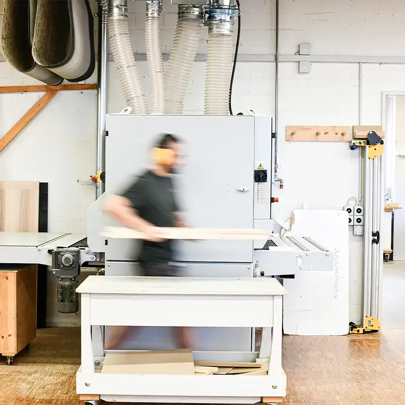 Schreiner mit Holz in der Hand vor Hobelmaschine