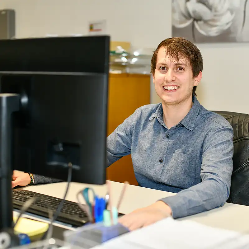 Mann arbeitet in der Administration am Computer und lacht