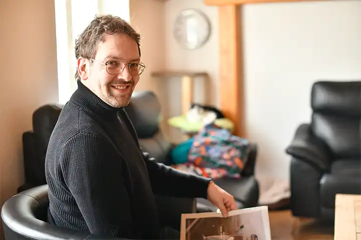 Mann mit schwarzem Pulli sitzt im Wohnzimmer und lächelt freundlich in die Kamera