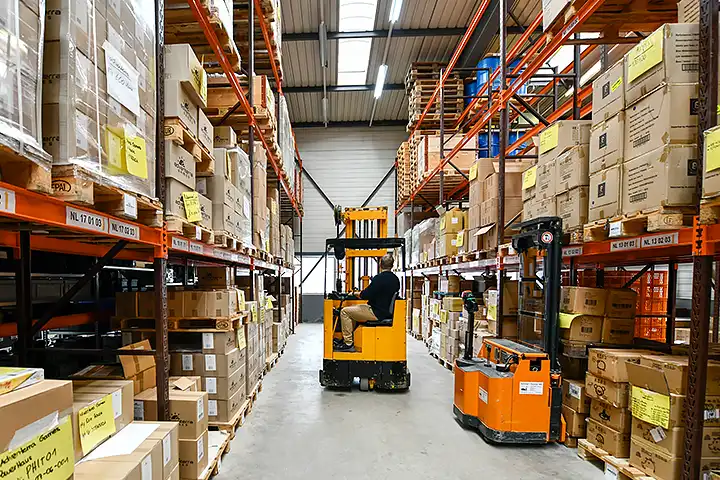 Logistiker fährt mit dem Stapler durch einen Gang im Hochregallager