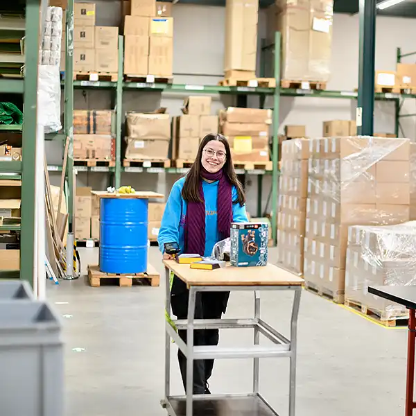Junge Frau arbeitet in der Logistik und schiebt einen Wagen zum Rüsten