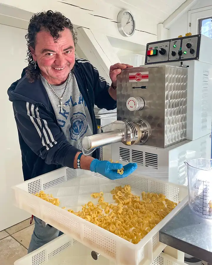 Mann mit lockigem Haar stellt an einer Maschine Teigwaren her