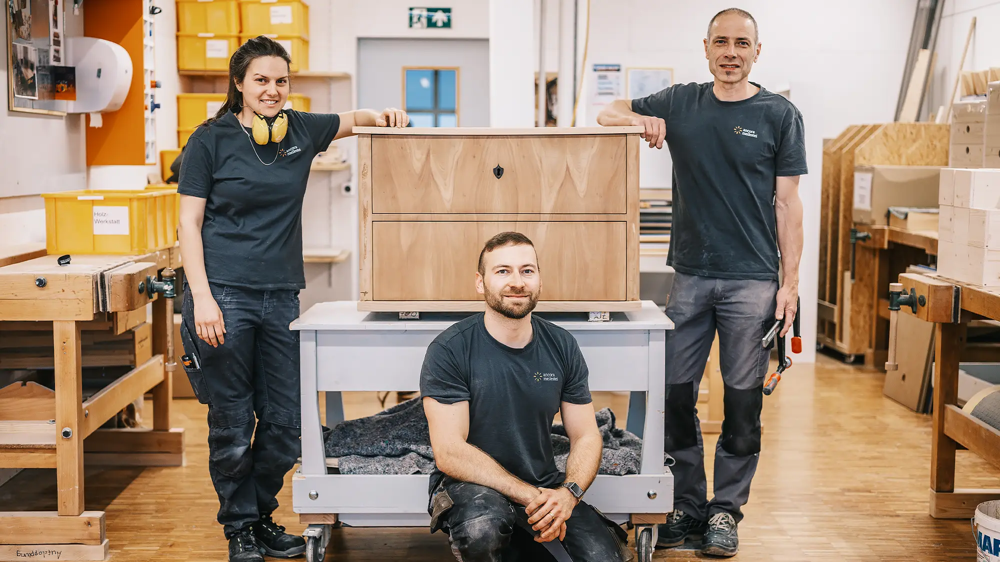 Drei Menschen aus der Holzwerkstatt mit einer schönen Kommode